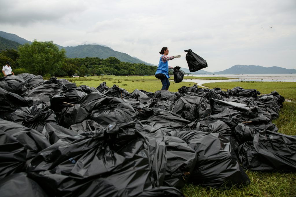 A worker sorts through bags of refuse washed ashore at the top of a beach in Hong Kong on July 10, 2016. Hong Kong's leader on July 10 blamed a huge rise in rubbish blighting the city's beaches on refuse washed ashore from the mainland, and pledged talks with Chinese authorities to stem the tide. / AFP PHOTO / ANTHONY WALLACE