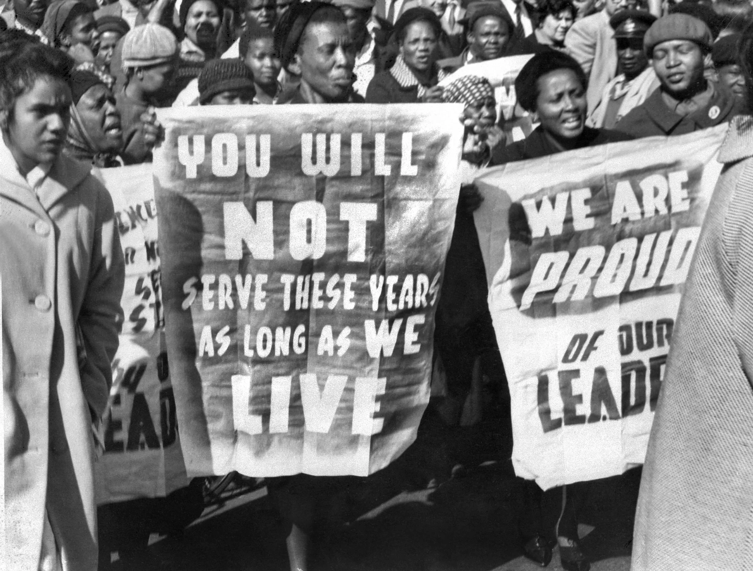 一九六四年六月十二日，法庭宣判曼德拉終身監禁，庭外支持者舉起標語：你必將釋放，只要我們仍然活着。另一標語：為我們的領袖感到自豪。